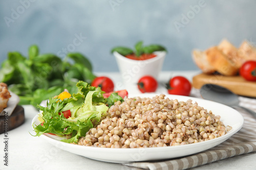 Tasty buckwheat porridge with salad on white wooden table. Space for text