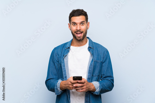 Handsome man over isolated blue background surprised and sending a message