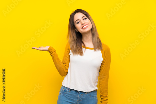 Pretty young woman over isolated yellow wall holding copyspace imaginary on the palm to insert an ad