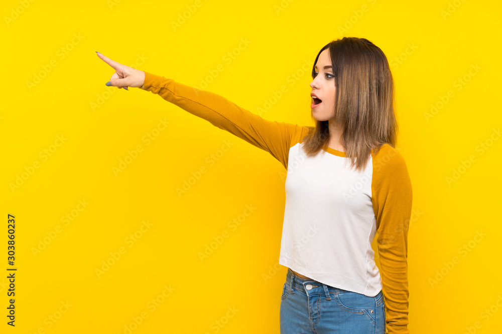 Pretty young woman over isolated yellow wall pointing away Pretty young woman over isolated yellow wall pointing away