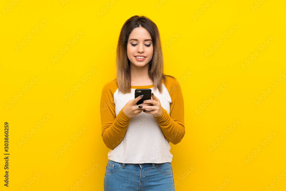 Pretty young woman over isolated yellow wall sending a message with the mobile Pretty young woman over isolated yellow wall sending a message with the mobile