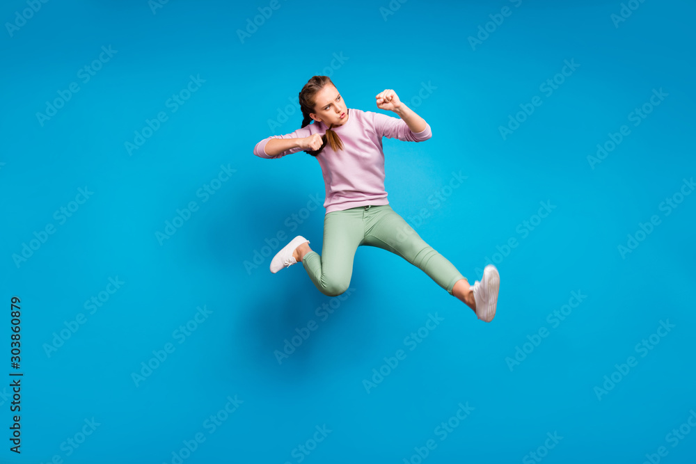 Full body profile side photo of concentrated funky youth girl jump train her fighting skills kick leg enemy wear modern clothes sweater isolated over blue color background Full body profile side photo of concentrated funky youth girl jump train her fighting skills kick leg enemy wear modern clothes sweater isolated over blue color background