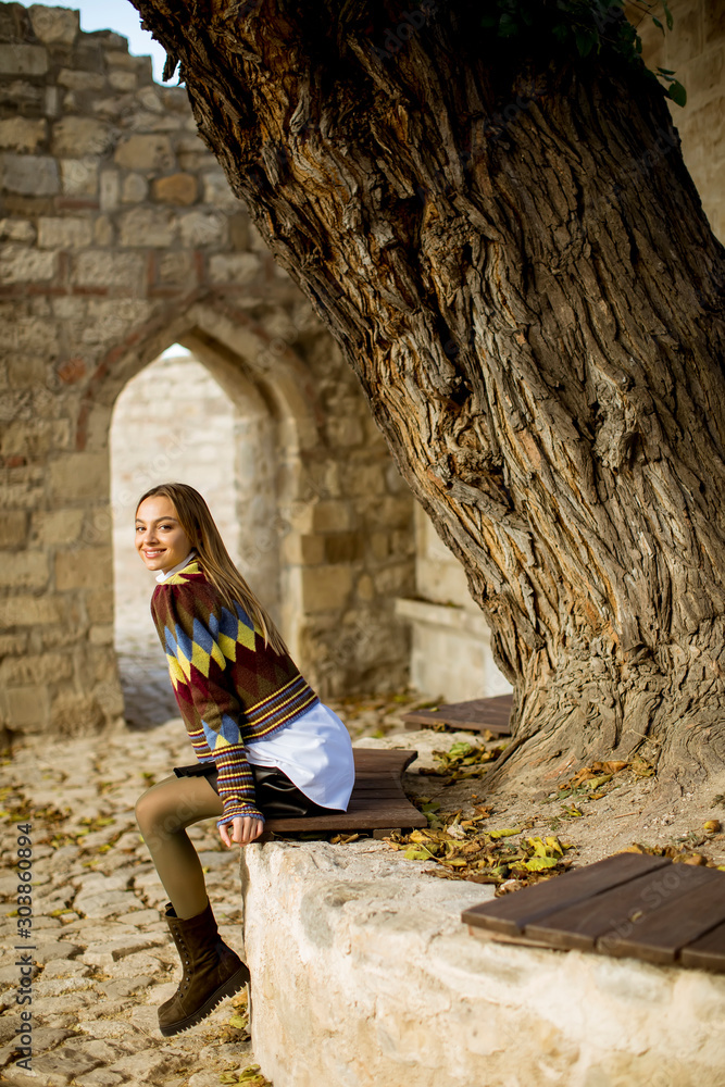 Young woman sitting on the bench watching yellow leaves tree in the autumn park Young woman sitting on the bench watching yellow leaves tree in the autumn park