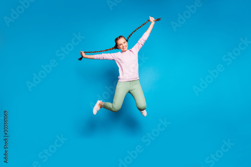 Full length photo of positive cheerful millennial girl jump hold her braids have fun wear casual style outfit white sneakers isolated over blue color background