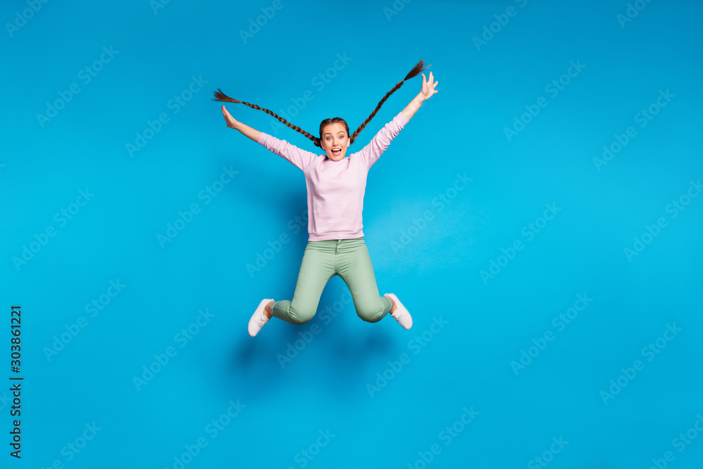 Full length photo of pretty crazy lady long braids flying jumping high rejoicing free time carefree mood wear casual pink pullover green pants isolated blue color background Full length photo of pretty crazy lady long braids flying jumping high rejoicing free time carefree mood wear casual pink pullover green pants isolated blue color background