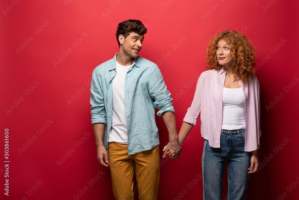 Φωτογραφία beautiful happy couple in casual clothes holding hands isolated on red