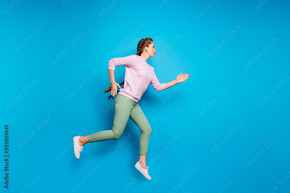 Full length profile photo of pretty lady long braids jumping high sports competition run to finish line wear casual pink pullover green pants isolated blue color background Full length profile photo of pretty lady long braids jumping high sports competition run to finish line wear casual pink pullover green pants isolated blue color background