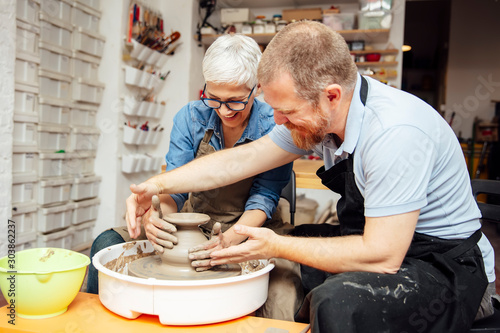 Senior woman spinning clay on a wheel with teacher at pottery class