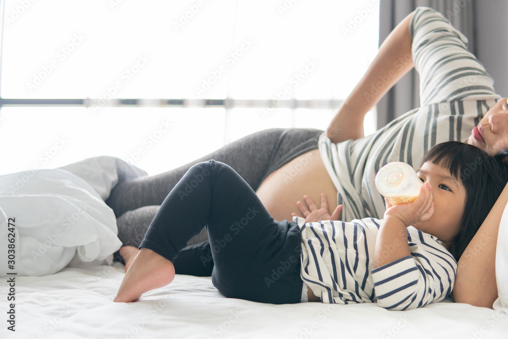Happy asian family. Mother and daughter are playing tablet relax and fun. Mom and girl watch gadget sitting on the bed in the bedroom. Happy asian family. Mother and daughter are playing tablet relax and fun. Mom and girl watch gadget sitting on the bed in the bedroom.