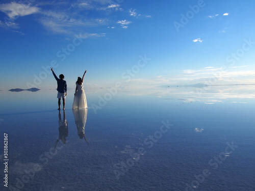 Bride and groom standing on a salt lake with reflections under a beautiful blue sky, Salar de Uyuni, Salar de Uyuni is the world's largest salt flat, Bolivia