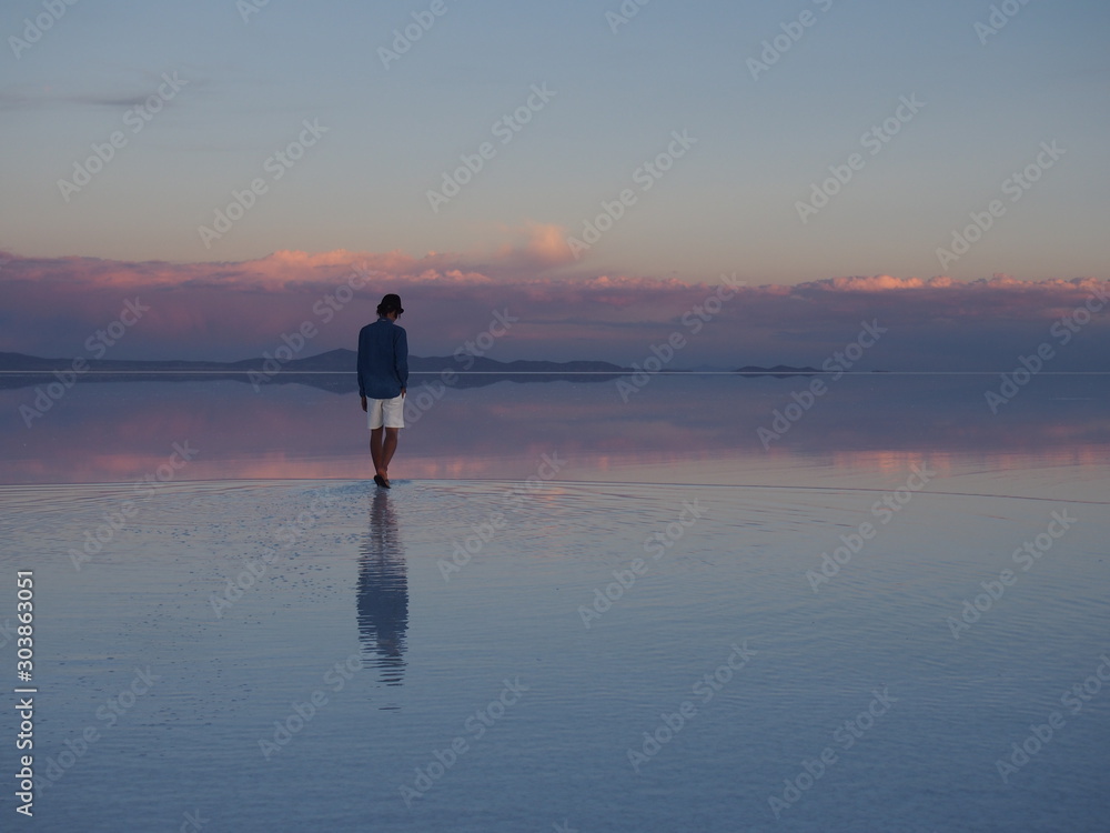 Φωτογραφία A groom walks through a salt lake reflecting the landscape under a sky tinged re