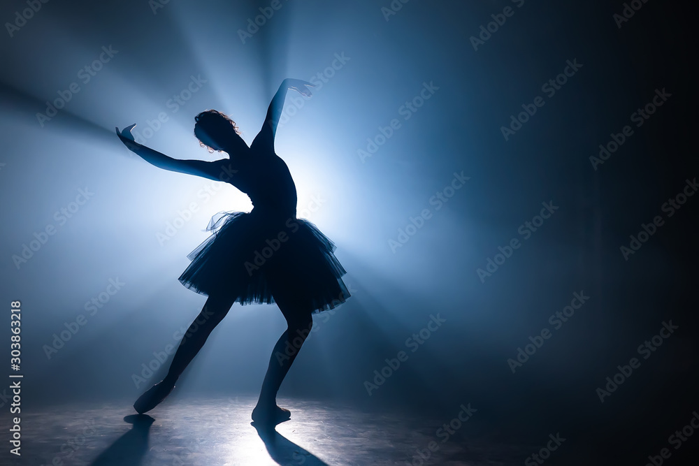 Ballerina in black tutu dress dancing on stage with magic blue light and smoke. Silhouette of young attractive dancer in ballet shoes pointe performing in dark. Copy space.