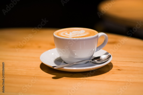 Ceramic cup in coffee shop with cappuccino on wooden empty table. Latte art. Morning drink. Caffeine.