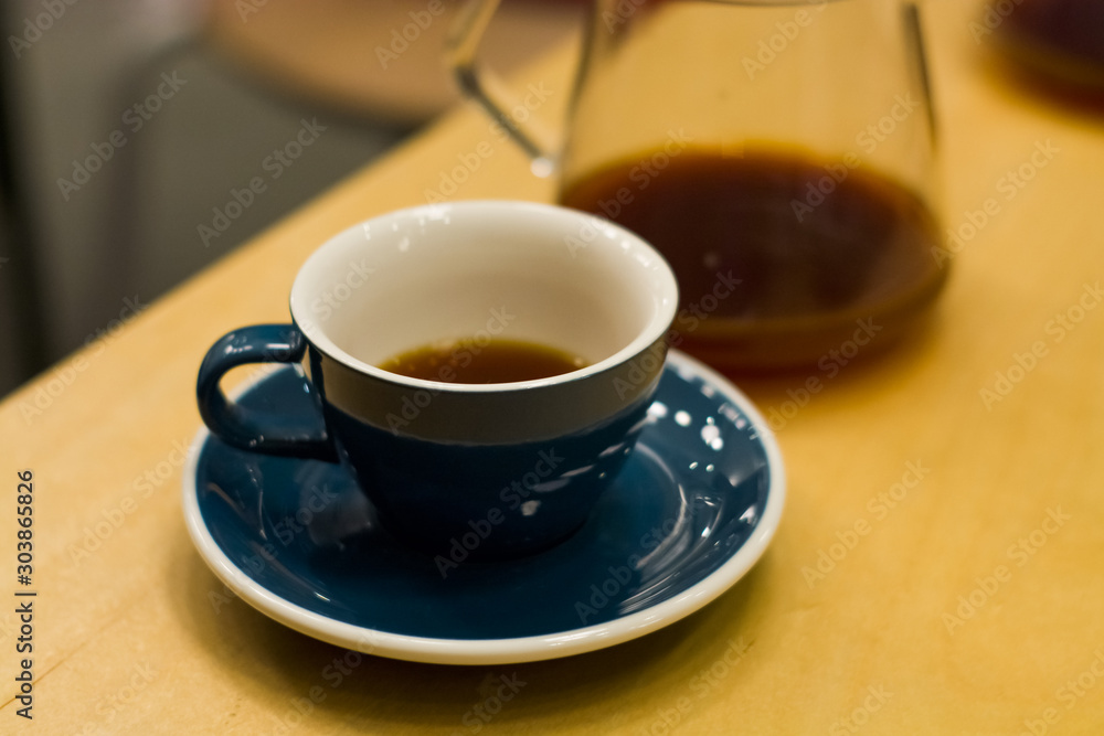 Blue ceramic cup with saucer in coffee shop on wooden table with strong, black, invigorating coffee. Americano. Morning drink. Jug. Ware.