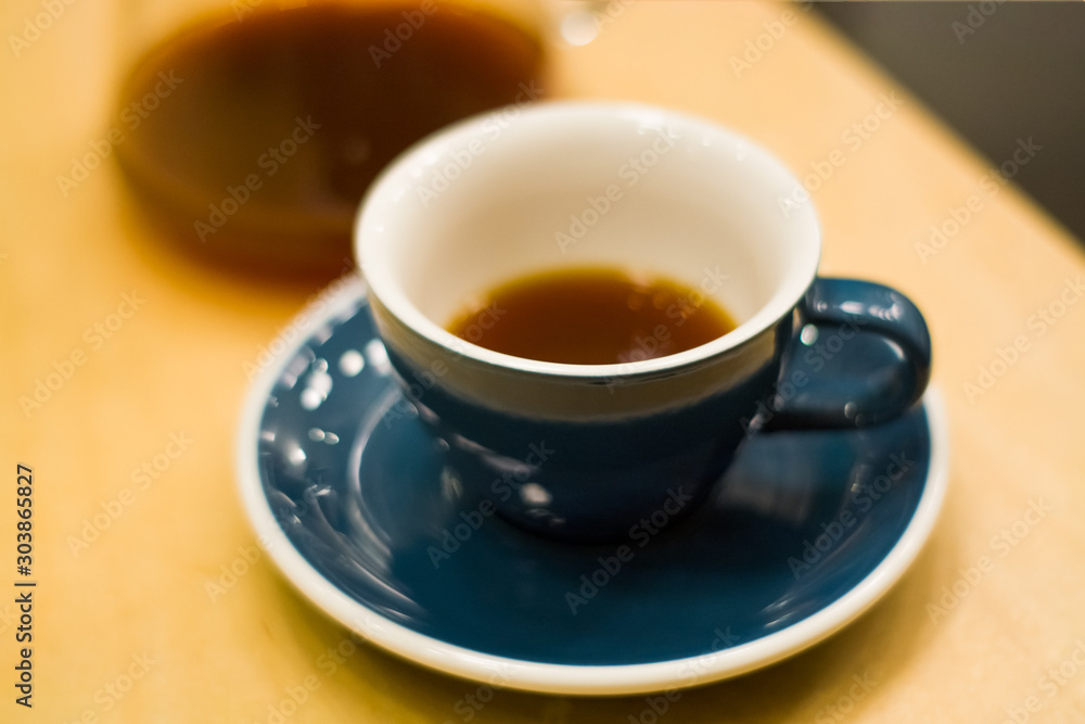 Blue ceramic cup with saucer in coffee shop on wooden table with strong, black, invigorating coffee. Americano. Morning drink. Jug. Ware. Blue ceramic cup with saucer in coffee shop on wooden table with strong, black, invigorating coffee. Americano. Morning drink. Jug. Ware.