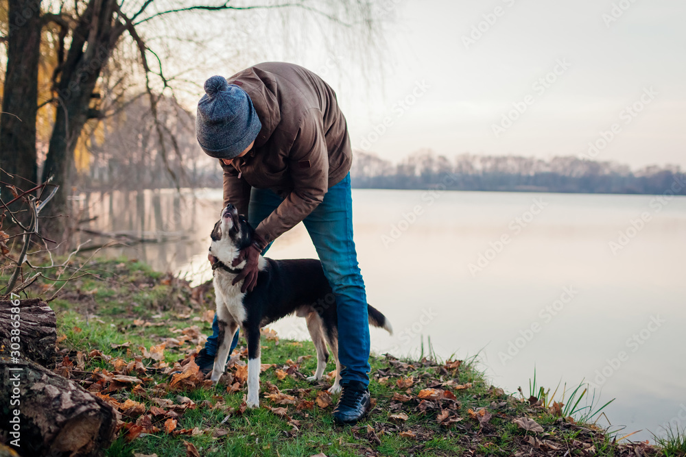 Man playing with dog in autumn park by lake. Happy pet having fun walking outdoors Man playing with dog in autumn park by lake. Happy pet having fun walking outdoors