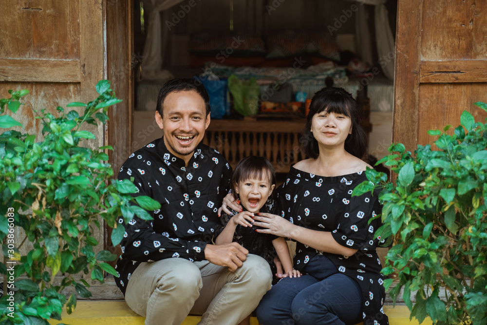 happy small asian family with daughter sitting in front door of a traditional country house