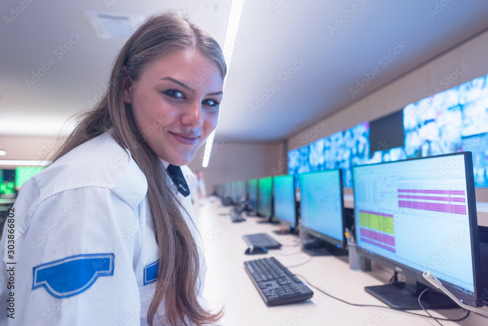 Security guard monitoring modern CCTV cameras in surveillance room. Female security guard in surveillance room. Smiling into camera. Security guard monitoring modern CCTV cameras in surveillance room. Female security guard in surveillance room. Smiling into camera.