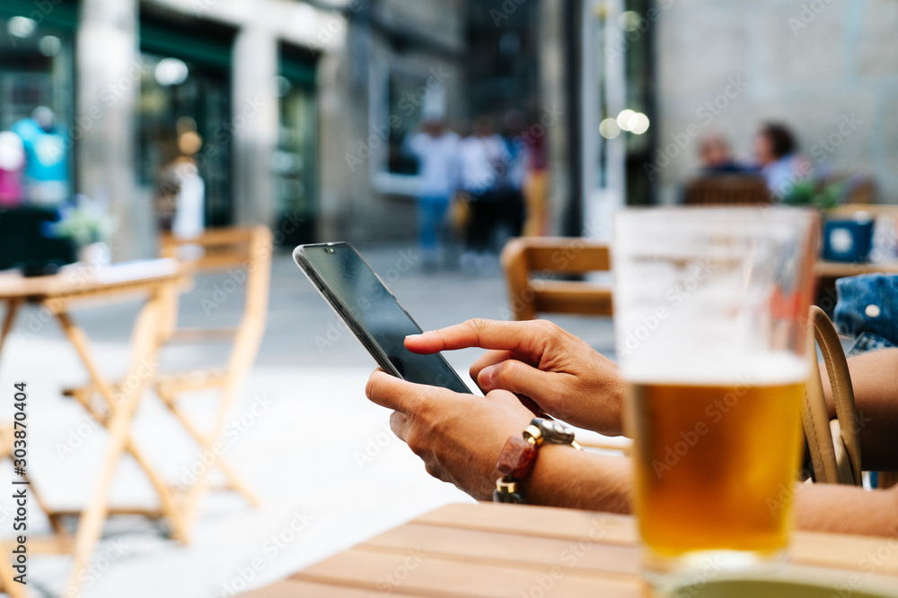 A woman's hand using the mobile phone on the terrace of a bar with a beer A woman's hand using the mobile phone on the terrace of a bar with a beer
