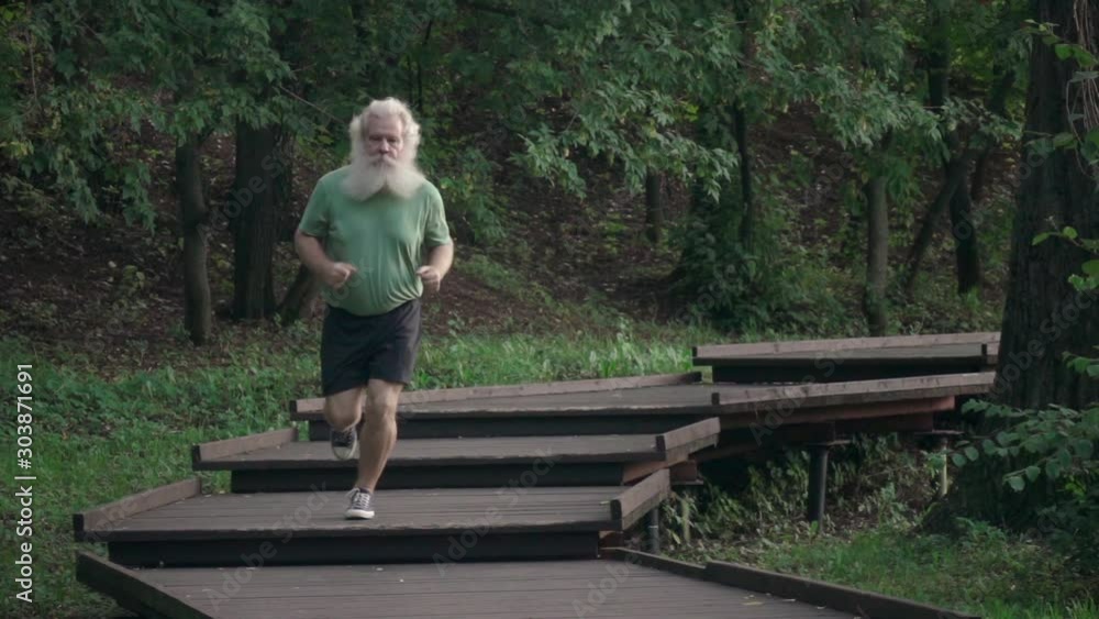 Sportive senior man running on wooden flooring with stairs at suburban area. Outdoor lifestyle portrait against natural green tree background. Active leisure. Slow motion shot. Sportive senior man running on wooden flooring with stairs at suburban area. Outdoor lifestyle portrait against natural green tree background. Active leisure. Slow motion shot.