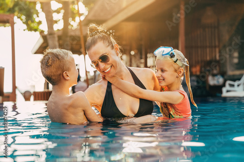 Laughing mother and kids playing together in a pool