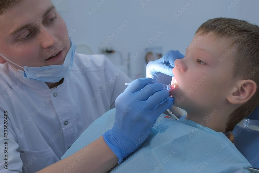 Dentist making fluoridation of child boy teeth after cleaning for protection. Doctor hygienist applying fluoride to teen teeth with brush. Covering teeth with fluoride gel in dentistry. Cure concept. Dentist making fluoridation of child boy teeth after cleaning for protection. Doctor hygienist applying fluoride to teen teeth with brush. Covering teeth with fluoride gel in dentistry. Cure concept.
