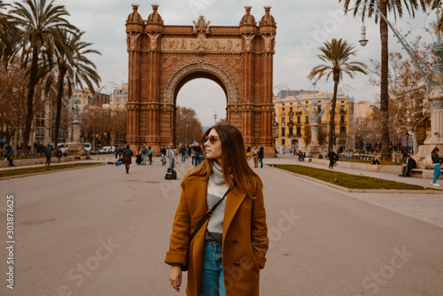 BARCELONA, SPAIN, January 17,2019.  Girl on the background the arch of Triumph in Barcelona. Cute young girl posing in autumn park. She is wearing mustard coat and glasses.  photo