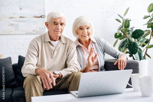 husband and smiling wife waving while video call in apartment