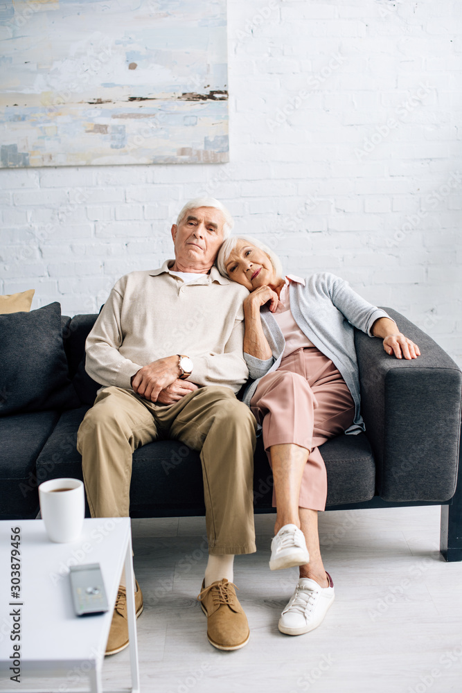 husband and wife sitting on sofa and watching sofa in apartment husband and wife sitting on sofa and watching sofa in apartment
