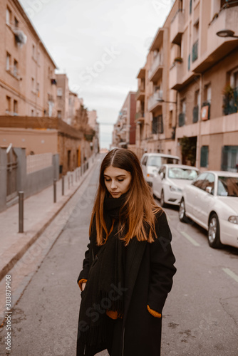 Modern Spanish streets in Barcelona.  Young and slim woman in  black jacket is walking away along the street.  © OlenaHalahan