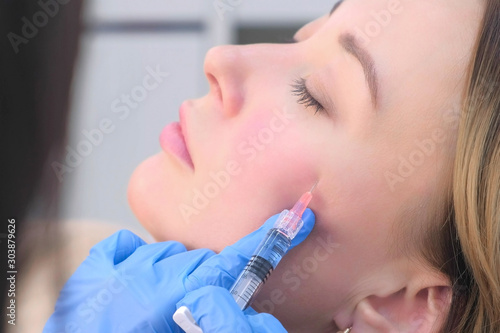 Doctor cosmetologist making injection with filler in mature woman patient cheek on face to moisturize and rejuvenate skin, side view. Beauty cosmetic procedure against wrinkle in clinic.