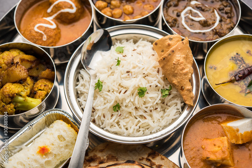 Indian vegetarian Food Thali or platter includes paneer butter masala, dal makhani / tarka, chole papad, kofta curry, gulab jamun, aloo-gobi sabji, chapati and rice with Bengali sweet served photo