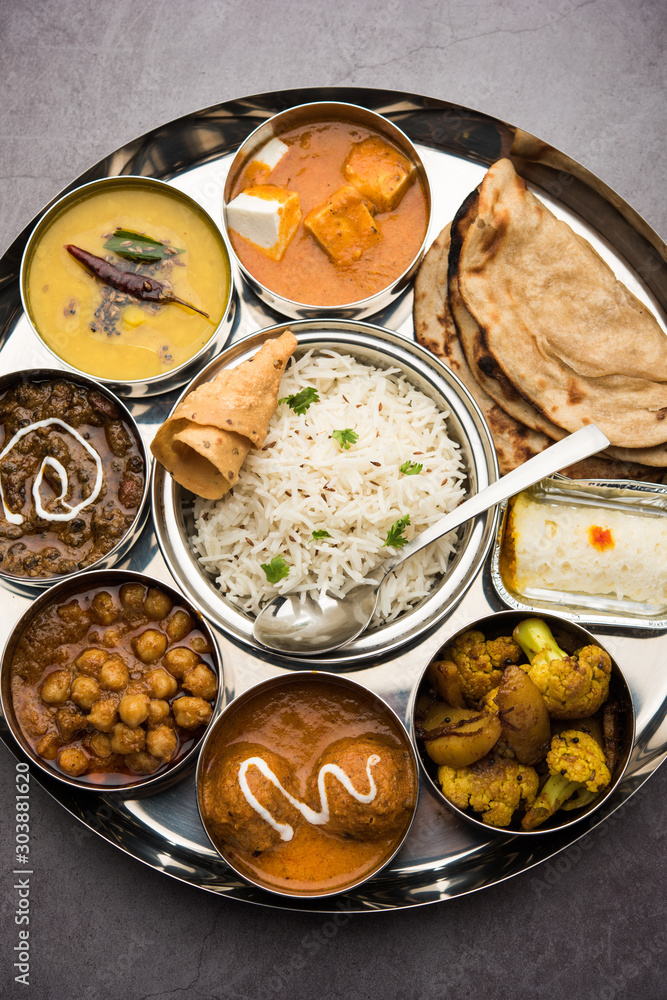 Indian vegetarian Food Thali or platter includes paneer butter masala, dal makhani / tarka, chole papad, kofta curry, gulab jamun, aloo-gobi sabji, chapati and rice with Bengali sweet served