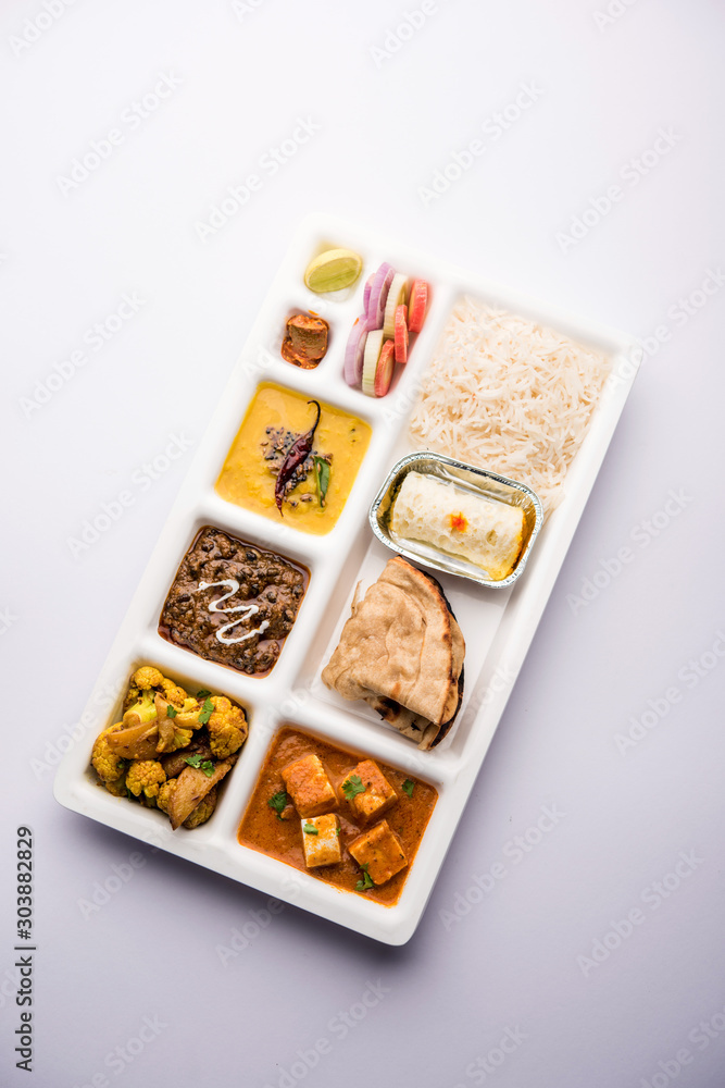 Indian vegaterian Food Thali or Parcel food-tray with compartments in which paneer, dal makhani / parka, aloo-gobi sabji, chapati and rice with Bengali sweet served