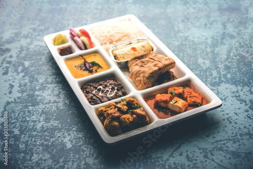 Indian vegaterian Food Thali or Parcel food-tray with compartments in which paneer, dal makhani / parka, aloo-gobi sabji, chapati and rice with Bengali sweet served