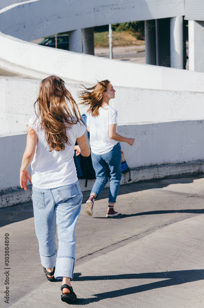 Two young women in white shirt and jeans running