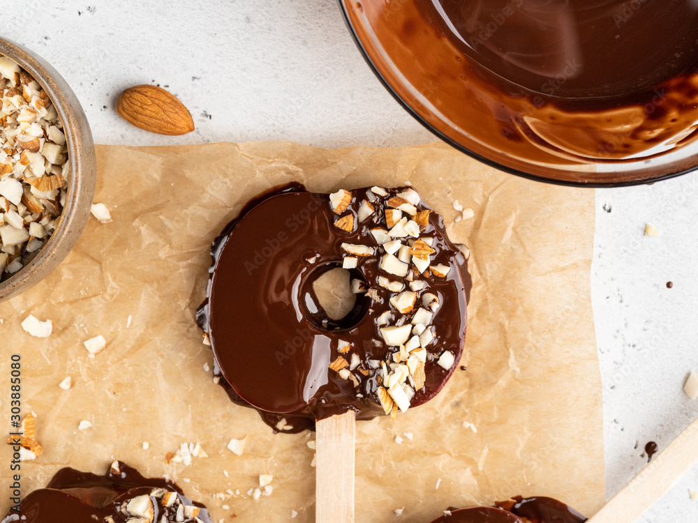Φωτογραφία Delicious fresh Red Apple slices in melted chocolate with chopped almond nuts on wooden popsickle sticks, White background, healthy dessert