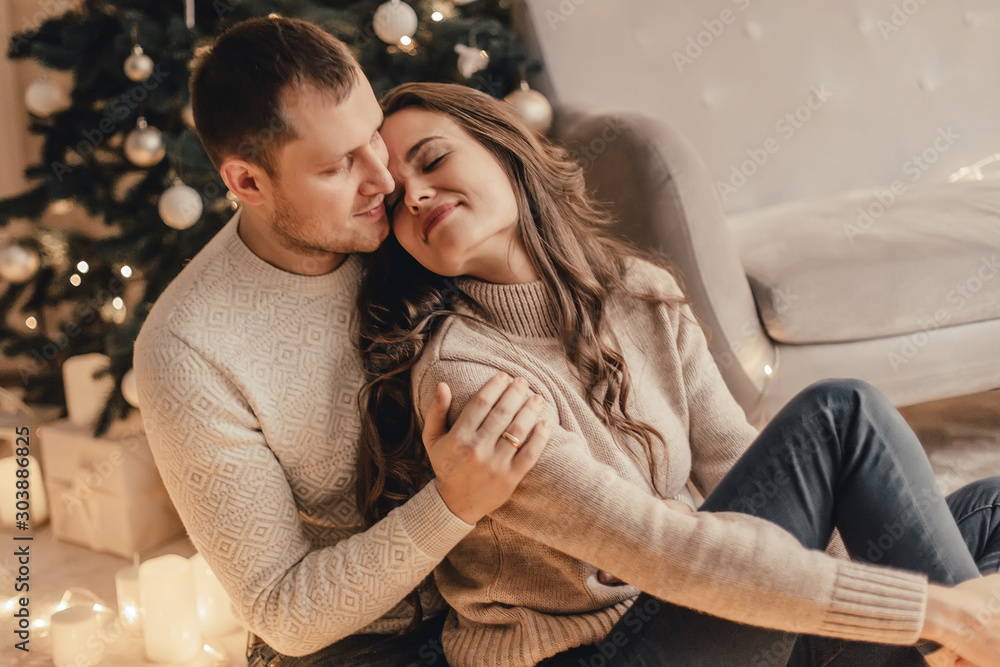 Beautiful young couple sitting on the floor and celebrating new year in front of Christmas tree. Beautiful young couple sitting on the floor and celebrating new year in front of Christmas tree.