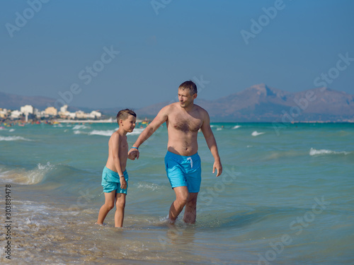 Cute European boy and his dad walking along beautiful seacoast. They are happy to spend their vacations together.