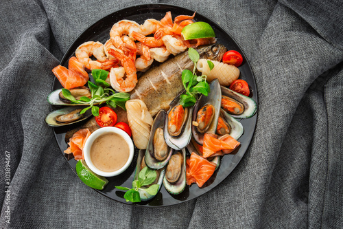 Obraz na płótnie Roasted Mixed Seafood Contain Mussels, prawns, salmon, Calamari Squids and Grilled Barracuda Fish Garlic with Spicy Chili Sauce. Isolated on gray Background. Seafood and meat platter. Horizontal w salonie