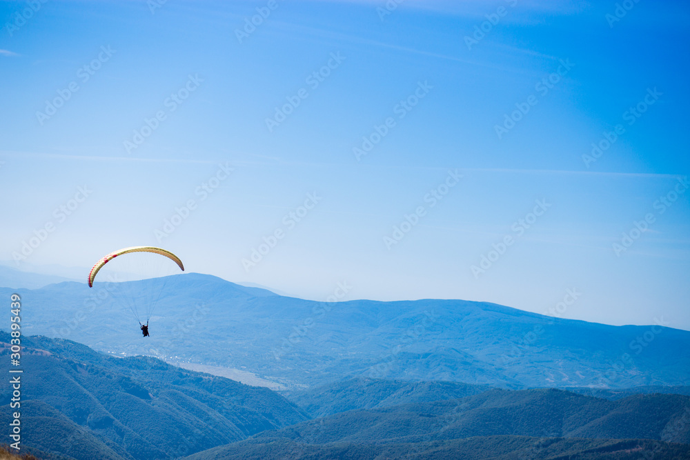 Paraglide silhouette flying over mountain peaks, beautiful rays of light in high mountain valley on background Paraglide silhouette flying over mountain peaks, beautiful rays of light in high mountain valley on background