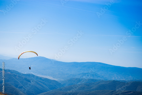 Paraglide silhouette flying over mountain peaks, beautiful rays of light in high mountain valley on background