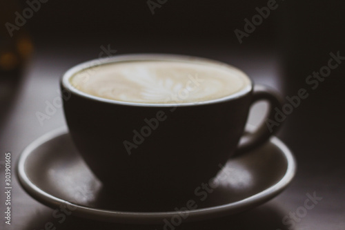 Large, black, ceramic cup of cappuccino close-up without focus. A black ceramic cup stands on a black wooden table