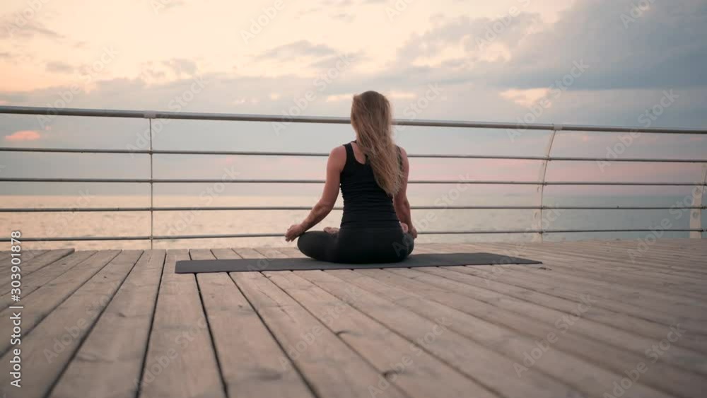 woman meditating on a beach near sea sitting on yoga mat in relaxing pose woman meditating on a beach near sea sitting on yoga mat in relaxing pose