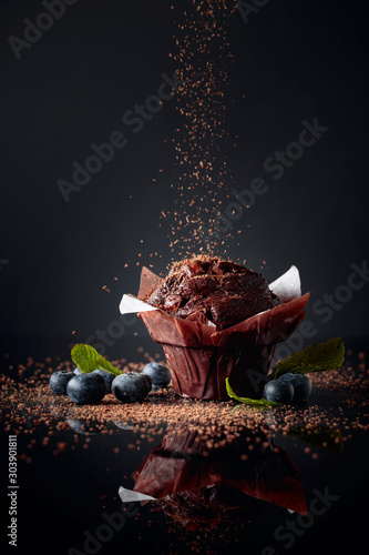 Fotografiet Chocolate muffin sprinkled with chocolate crumbs on a black reflective background