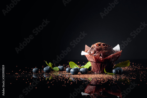 Obraz na plátně Chocolate muffin sprinkled with chocolate crumbs on a black reflective background