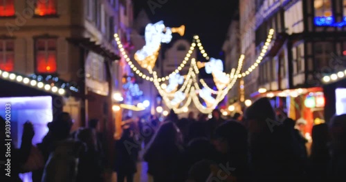 Large group of people pedestrians walking between the Christmas chalets market stalls during annual Christmas Market shopping gifts mulled wine sweets souvenirs defocused blurred silhouettes