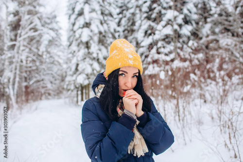 Portrait of a brunette woman in a yellow hat on a background of a winter forest. Closeup portrait of a girl in a snowy park.