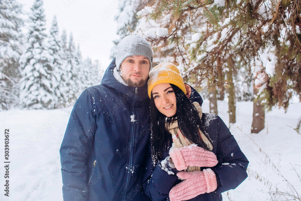 Obraz premium loving couple walks through the winter forest and plays with snow in cold weather. young couple is walking in a winter park. guy and girl in dark blue jackets. Winter forest. Active winter holidays.