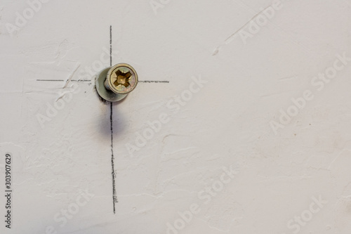 Metal screw with plastic dowel in white concrete wall for mounting. Pencil marking lines. Copy space.